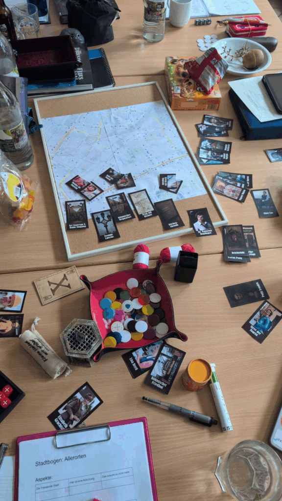 Ein Spieltisch mit Würfeln, Markern, Notizzetteln, vielen kleinen Bildern mit Dingen und Menschen drauf.